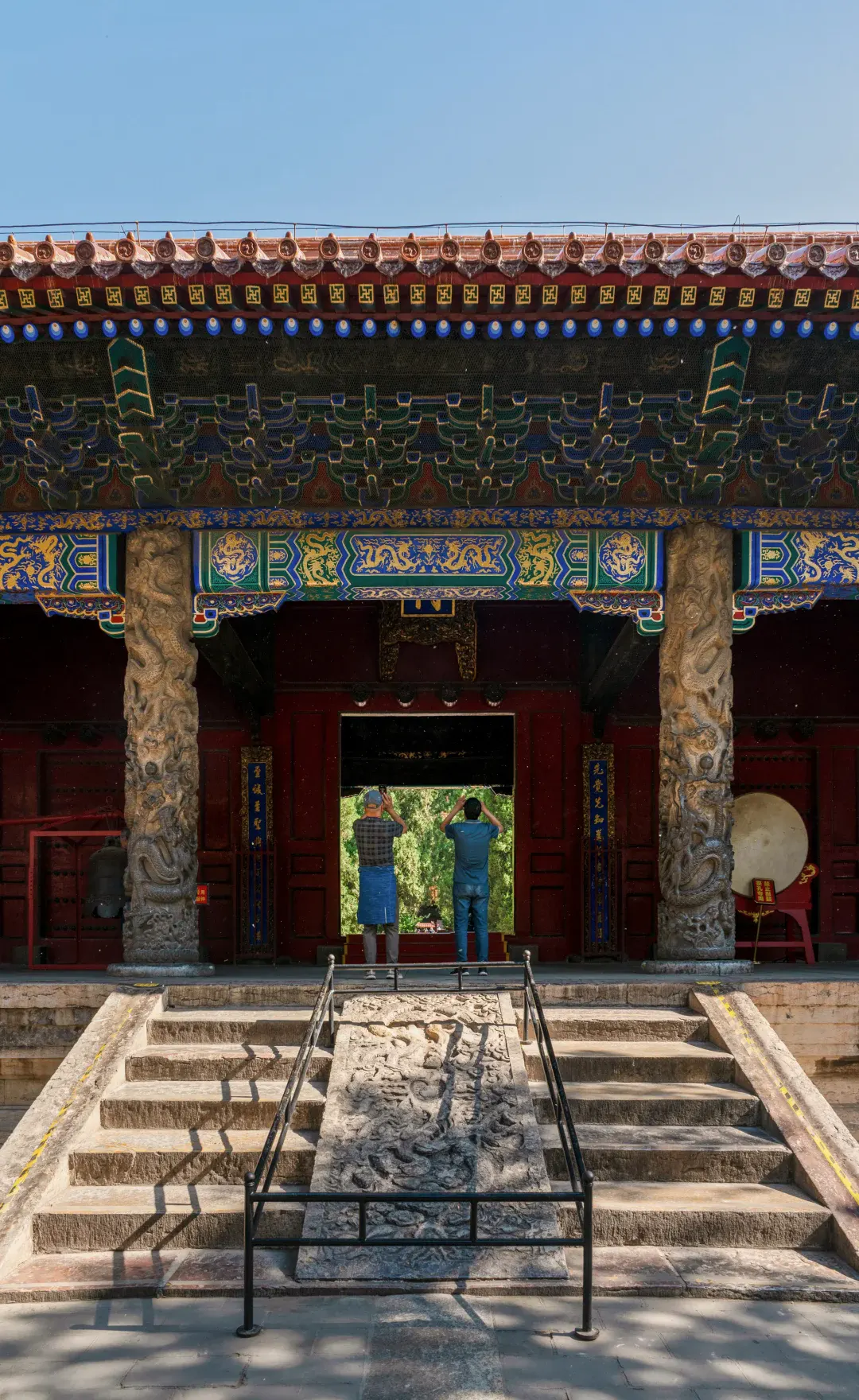 The Xingtan pavilion framed by an old carved stone support and visitors moving through the shaded threshold at Qufu