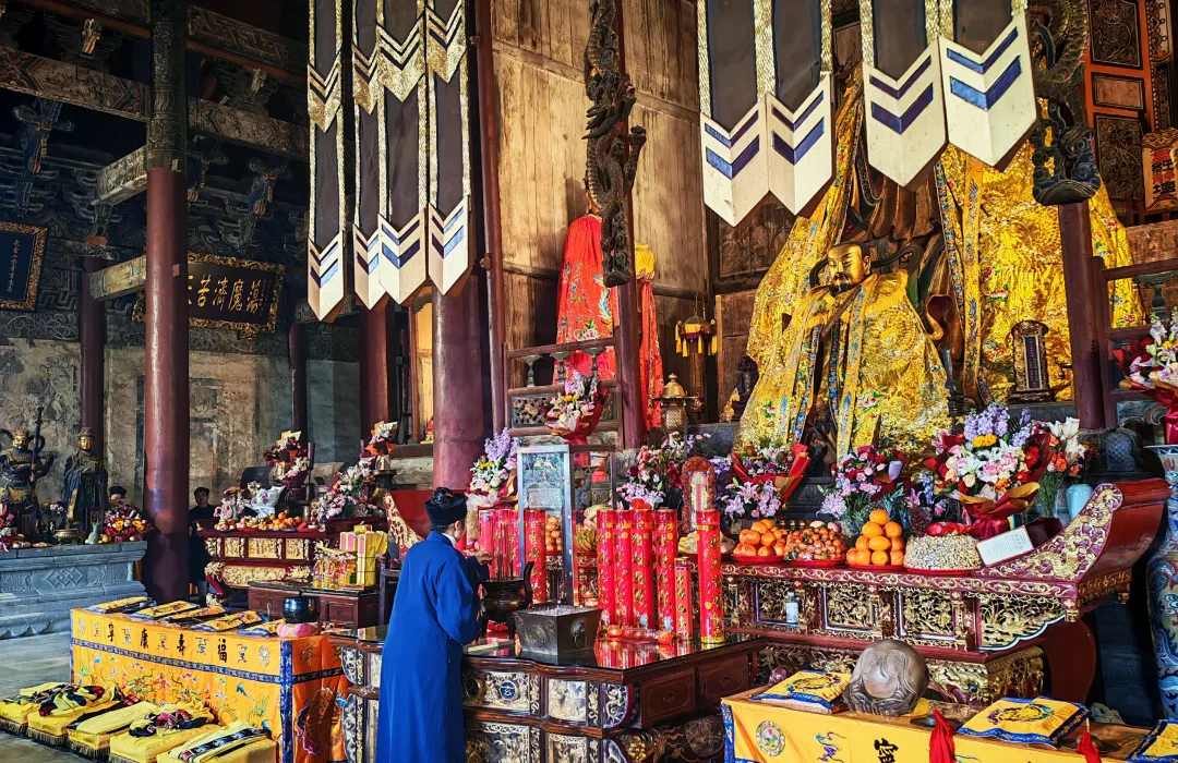 A Daoist practitioner standing before an active altar inside Purple Heaven Hall, surrounded by banners, offerings and liturgical furnishings