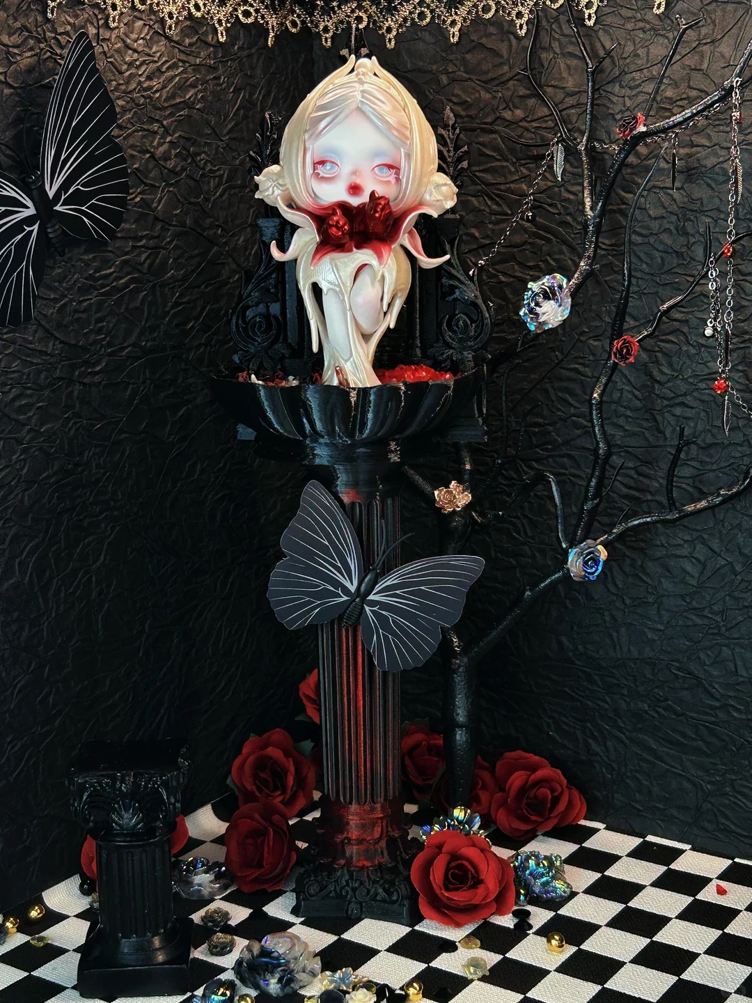 Authorized real SKULLPANDA figure staged on a black pedestal with red roses, butterflies, a branch and a textured black backdrop