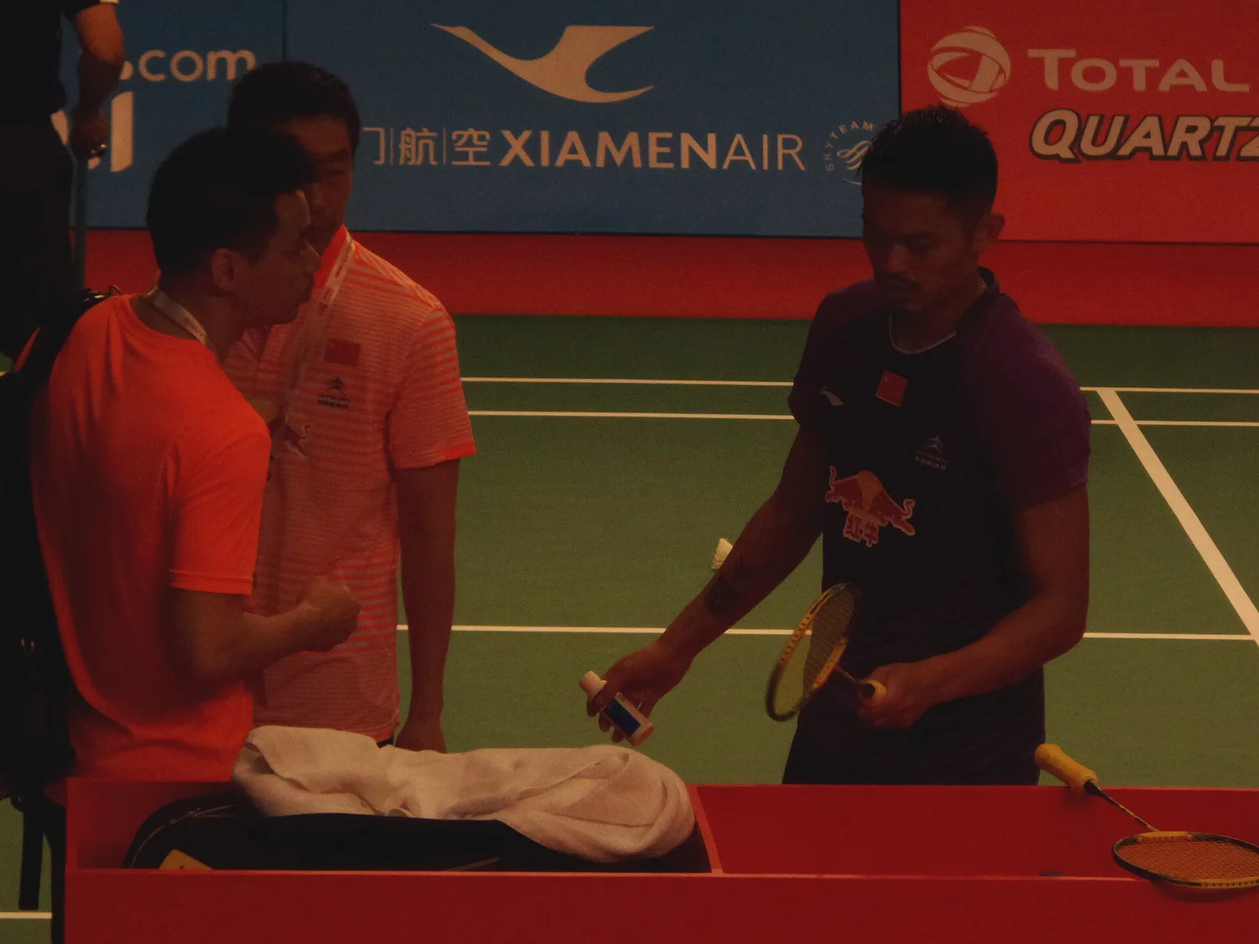 Lin Dan holds his racket and drink while speaking with coaches during the 2015 World Championships