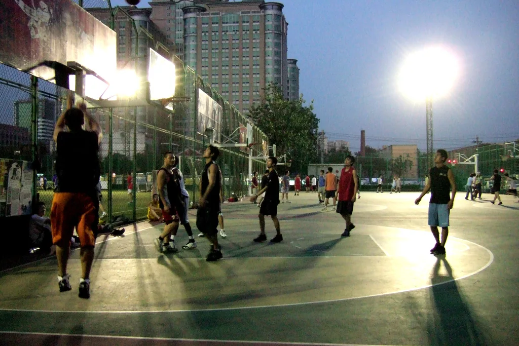 Players share a floodlit outdoor basketball court in a Beijing neighborhood after daylight