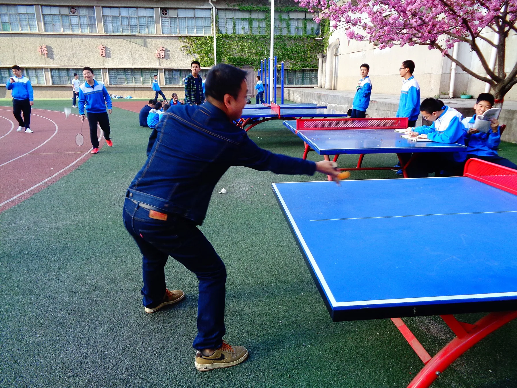 Students and an adult gather around several outdoor table-tennis tables in a Xi'an schoolyard