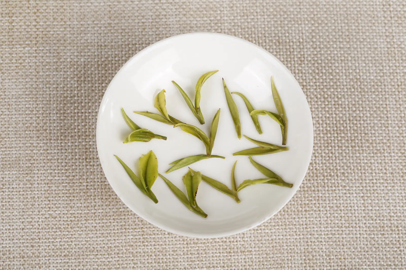 Tender green leaves arranged on a white plate, used to discuss picking scale and leaf form without claiming Dongting origin