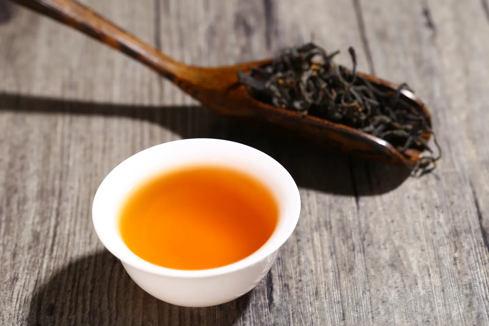 Dark twisted black-tea leaf beside an amber cup