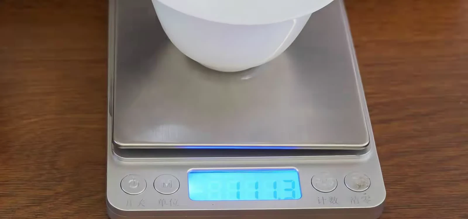 A digital scale reading 111.3 grams for water measured in a white porcelain gaiwan