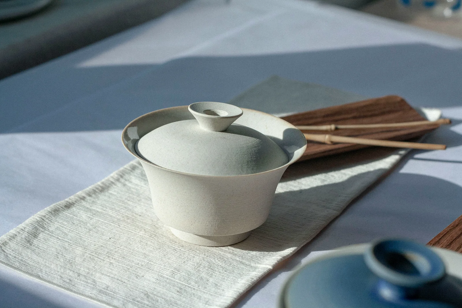 A white porcelain gaiwan with its bowl, lid and saucer clearly visible