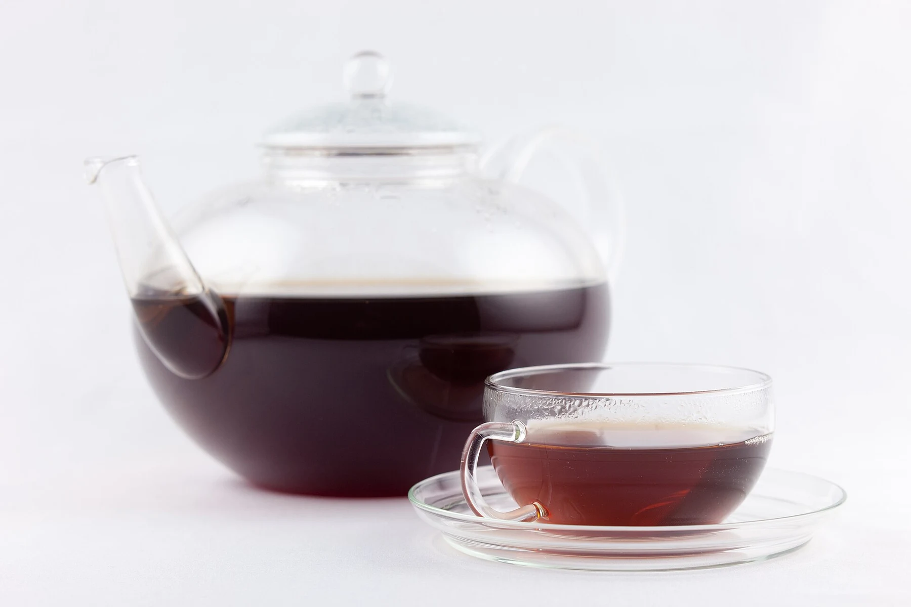 A close glass-teapot brewing study showing the vessel, leaves and serving cups together