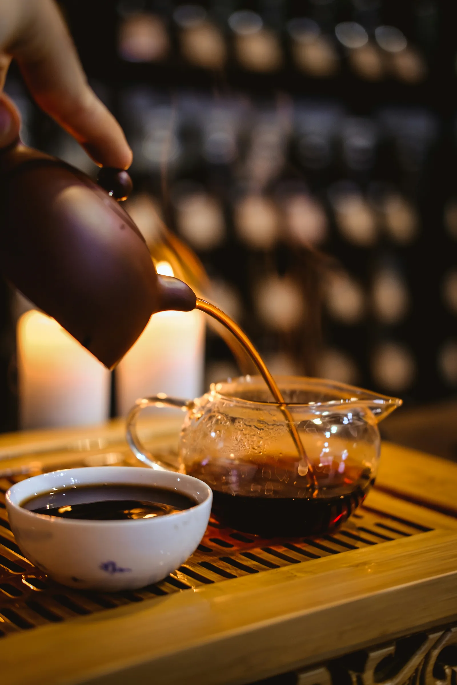 A dark teapot completing a continuous decant into a glass pitcher, making the stopping action visible