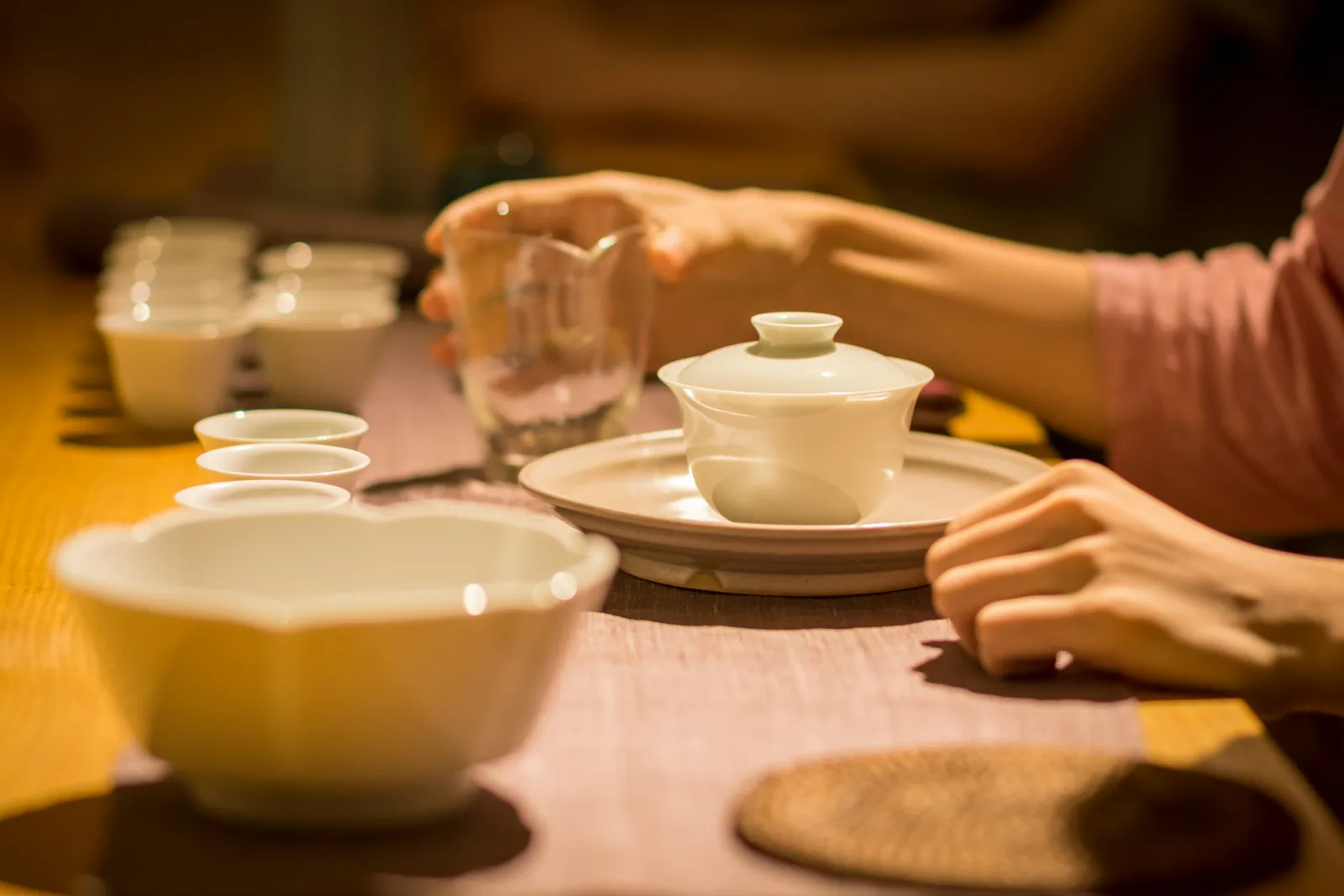 Hands holding a white gaiwan beside small cups during a real gongfu tea session