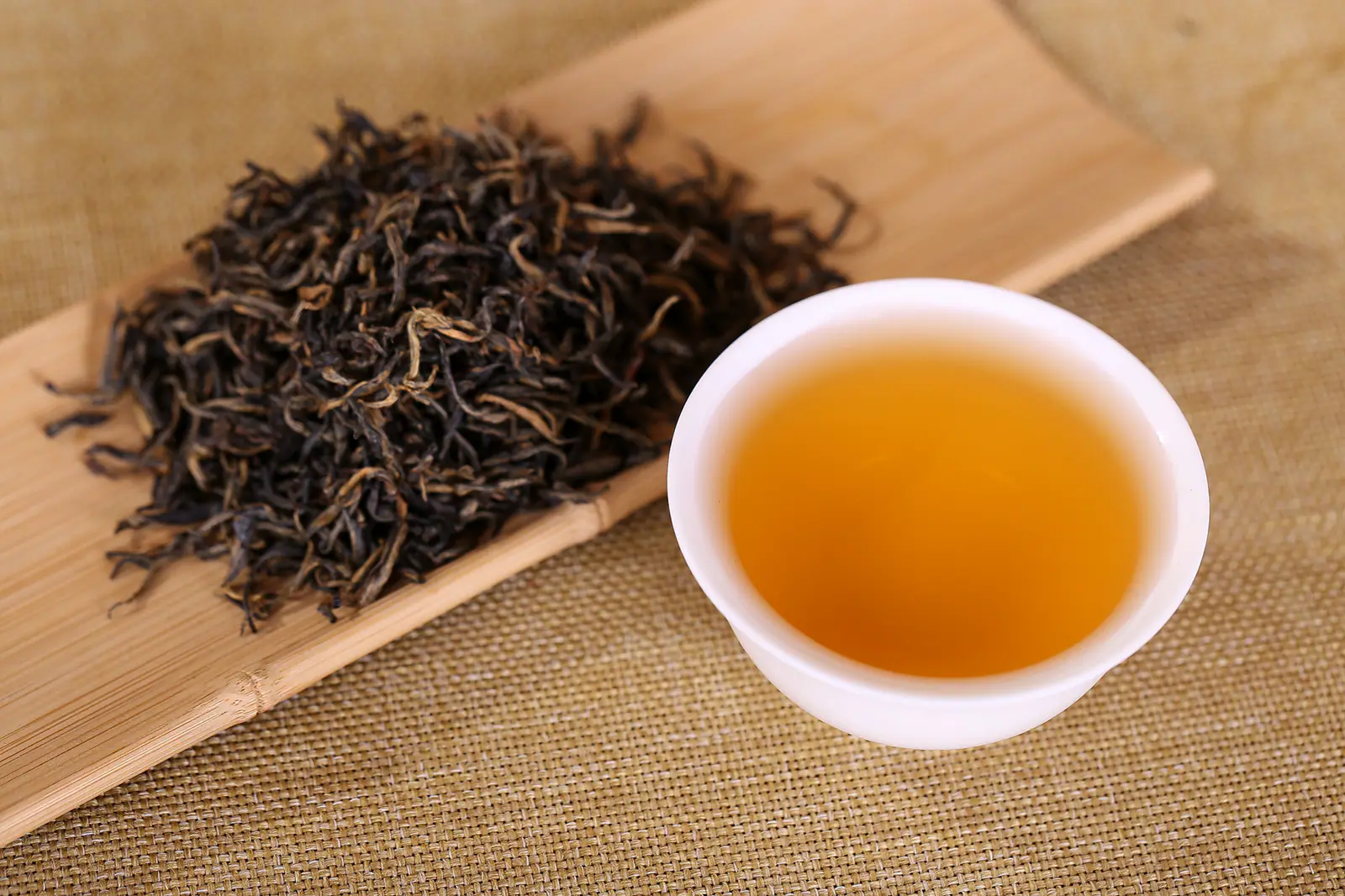 Fine dark tea leaves beside clear amber liquor, showing Keemun's leaf-and-cup relationship