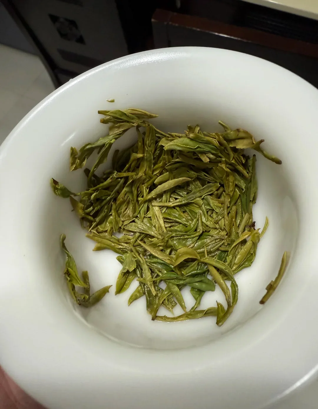 Opened Longjing tea leaves spread in a white bowl after tasting