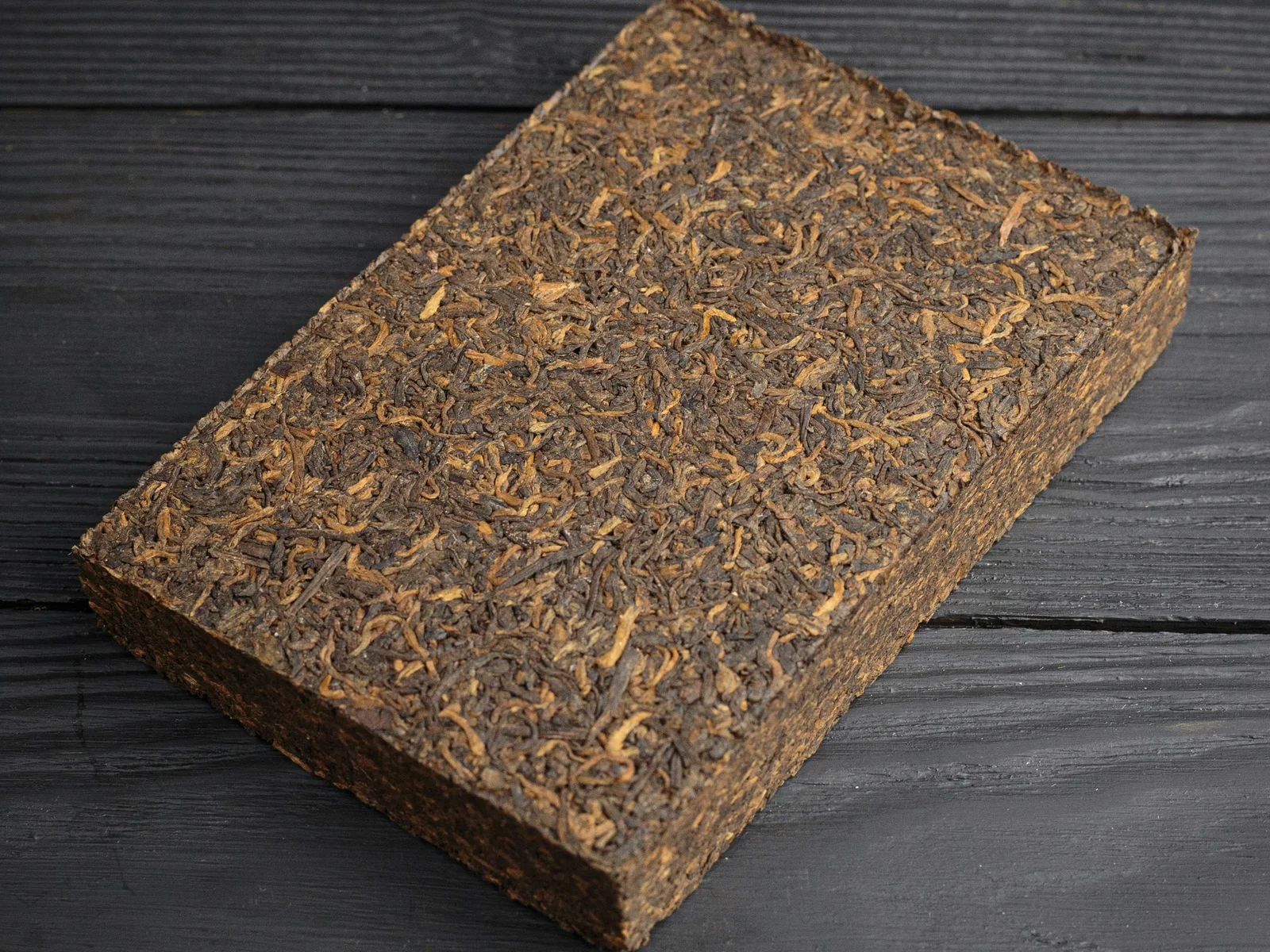 A real compressed dark-tea brick whose edge and layered breakage make the side-entry problem visible