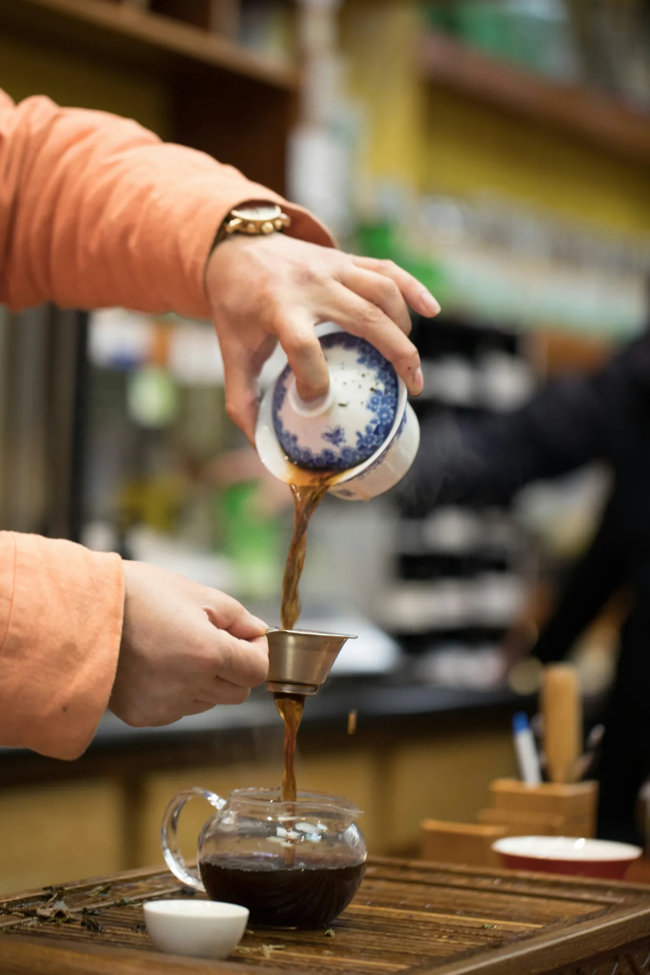 A real gaiwan being emptied through a strainer into a glass fairness pitcher in one continuous pour