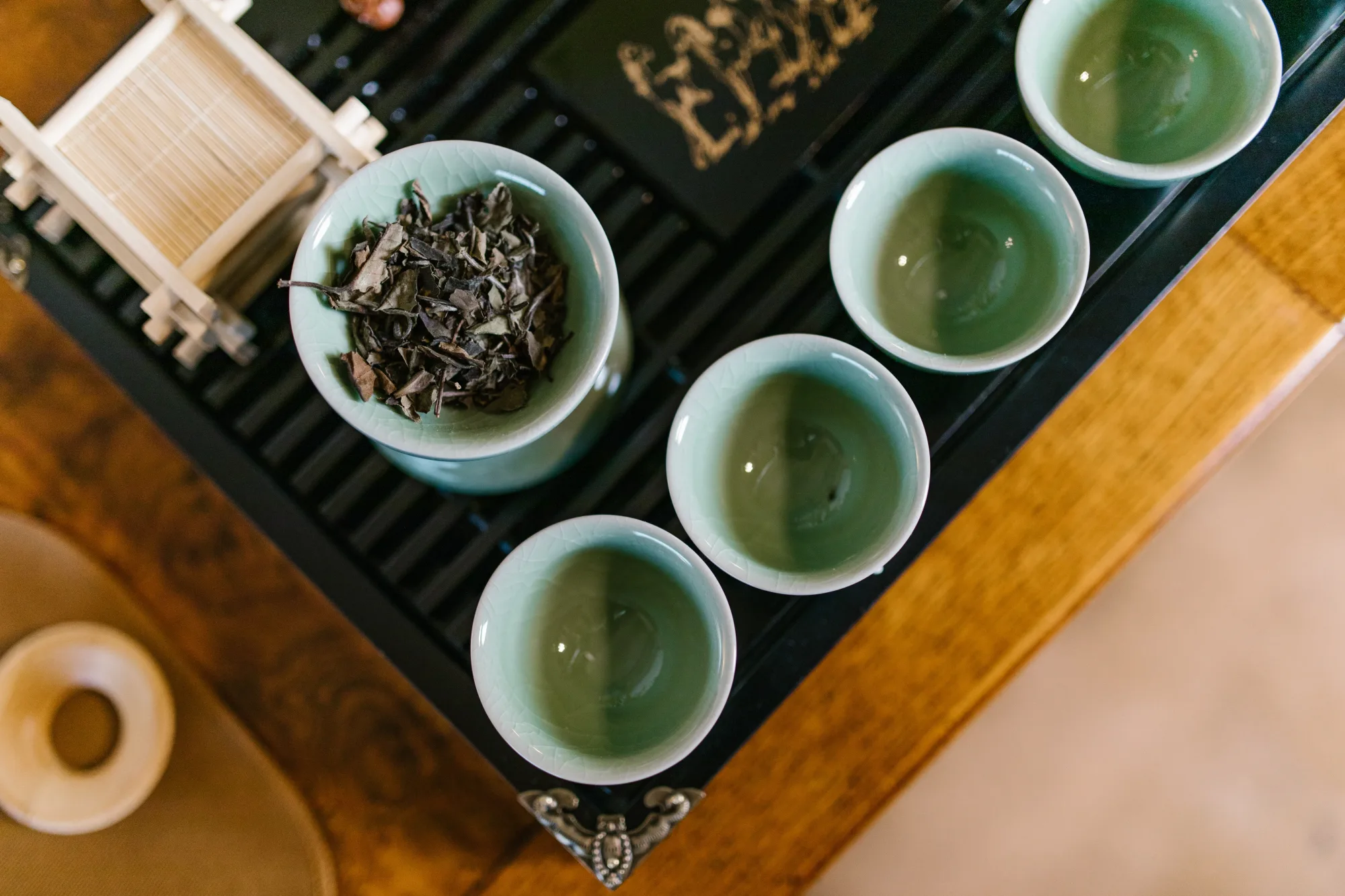 A real loose broad-leaf tea sample beside porcelain cups, showing stems, leaf size and the ordinary handful rather than a styled cake surface