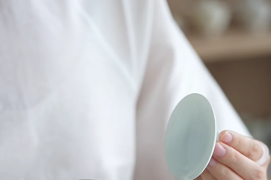 A hand showing the thin rim and pale glazed interior of a porcelain Chinese tea cup