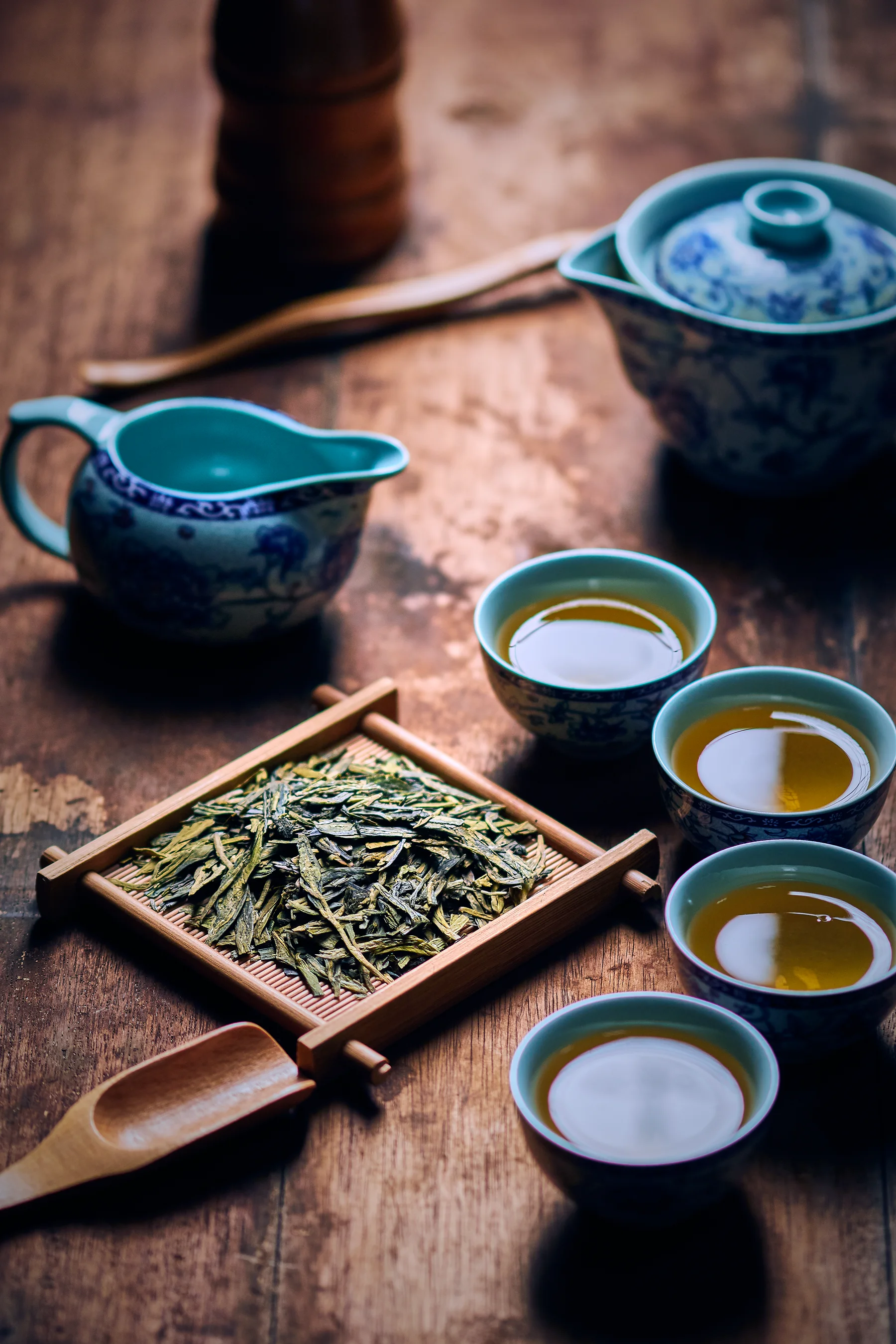 Several blue porcelain Chinese tea cups beside loose green tea and a lidded brewing bowl