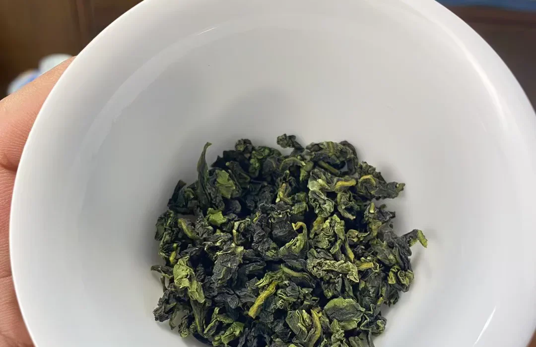 A greener light-fragrant Tieguanyin dry-leaf sample held in a white porcelain bowl