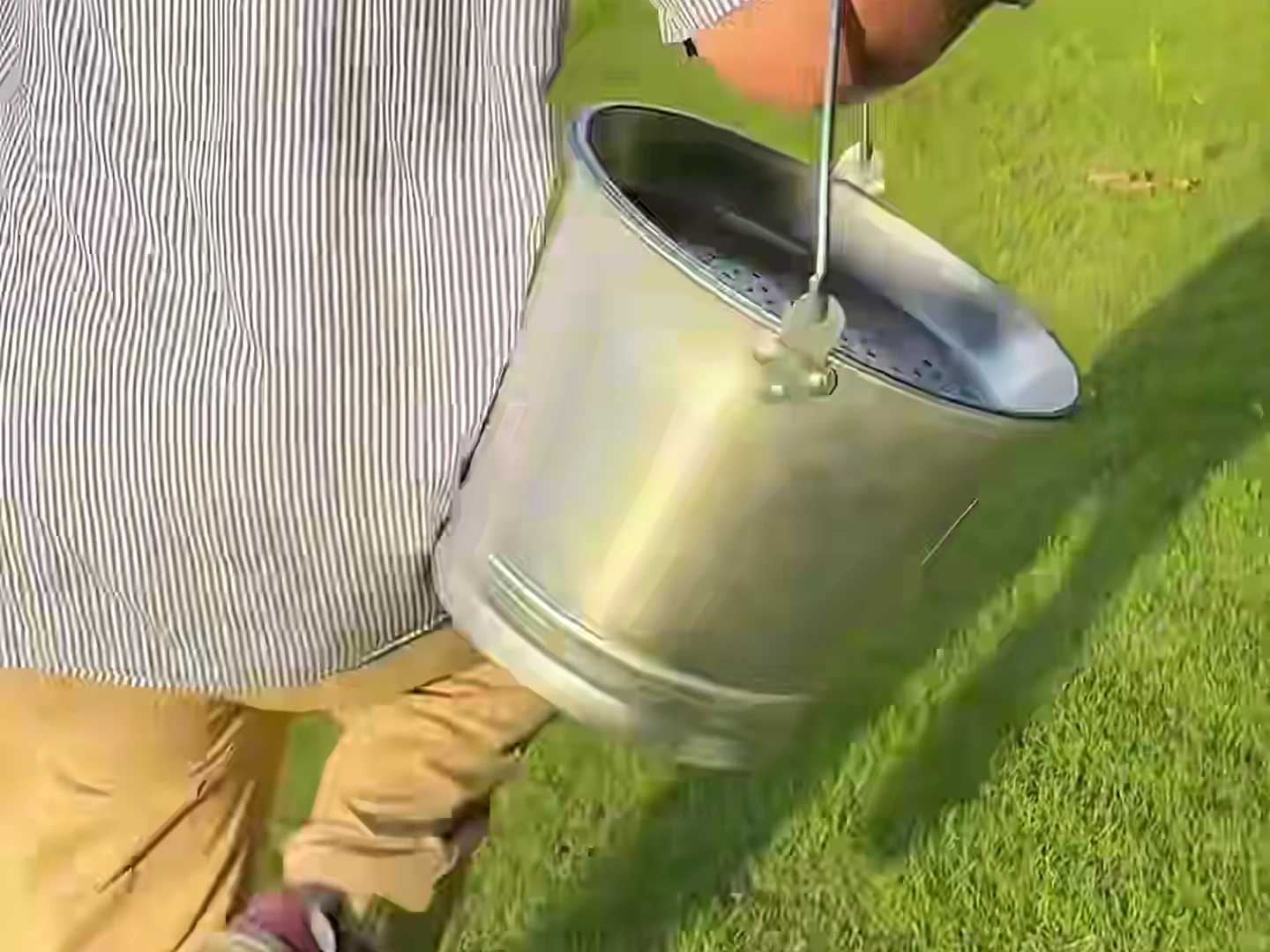A handled metal container being carried outdoors