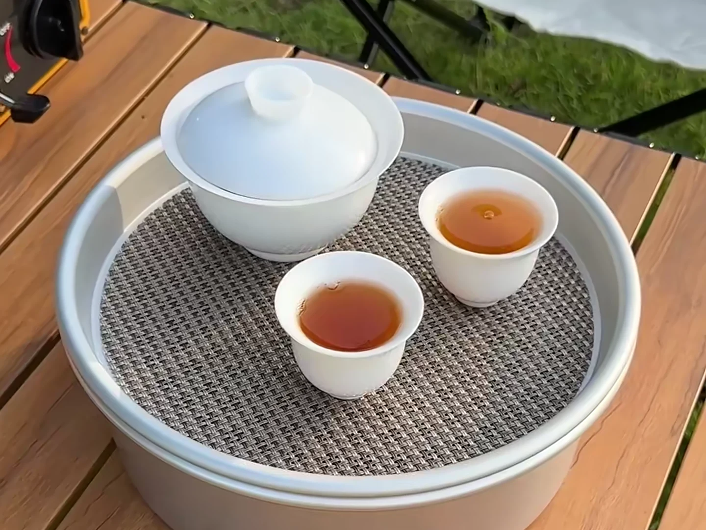 A gaiwan and two cups served on the insert of a handled outdoor container