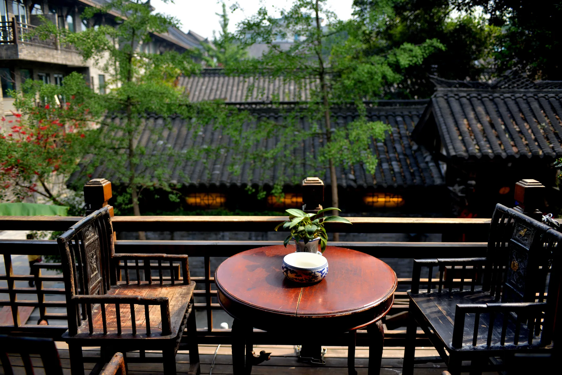 Wooden chairs and a tea table face tiled roofs from a Chengdu teahouse balcony
