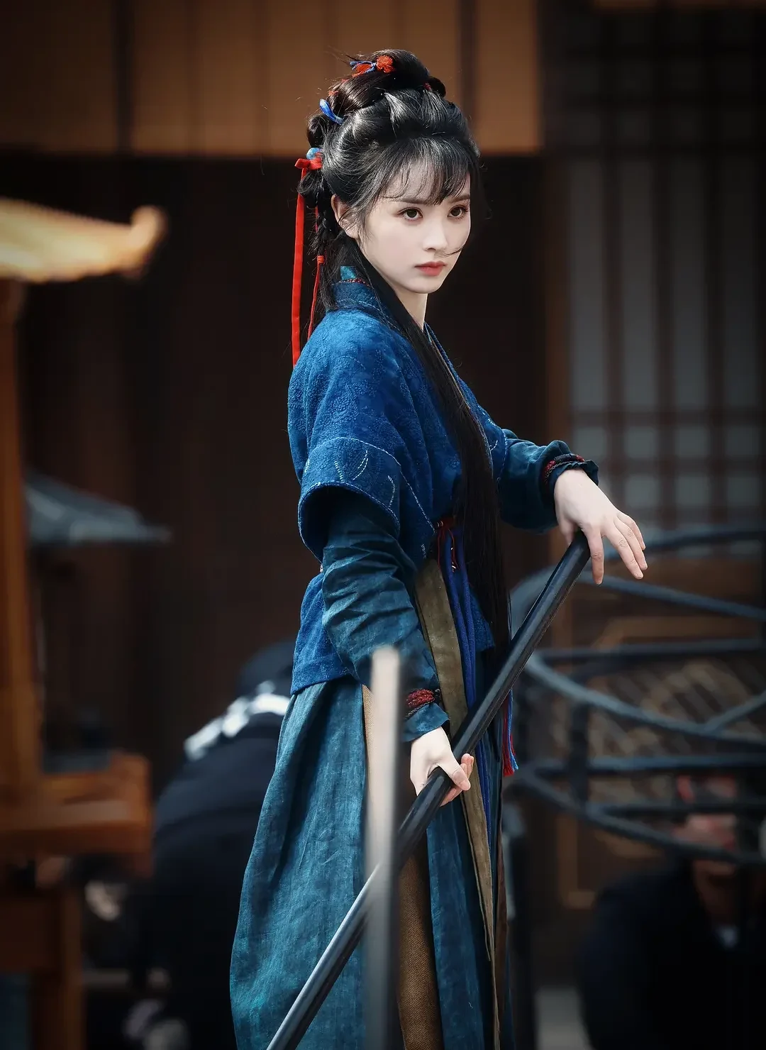 Fan Changyu holding a long-handled tool in blue work clothes, showing the role's physical vocabulary before courtly spectacle