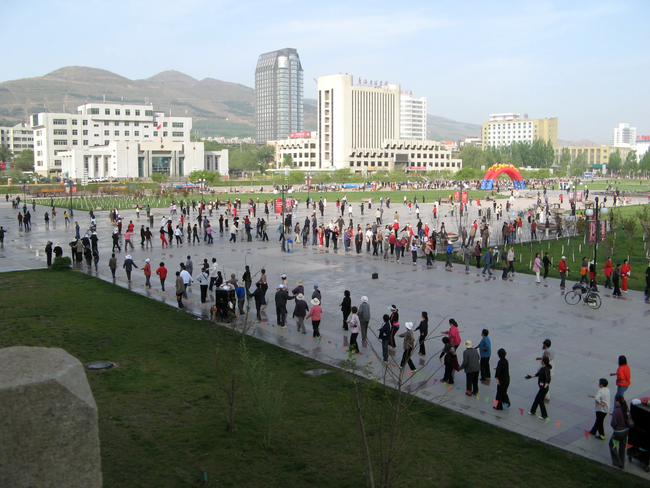 Several morning exercise groups moving across a public park in Xining
