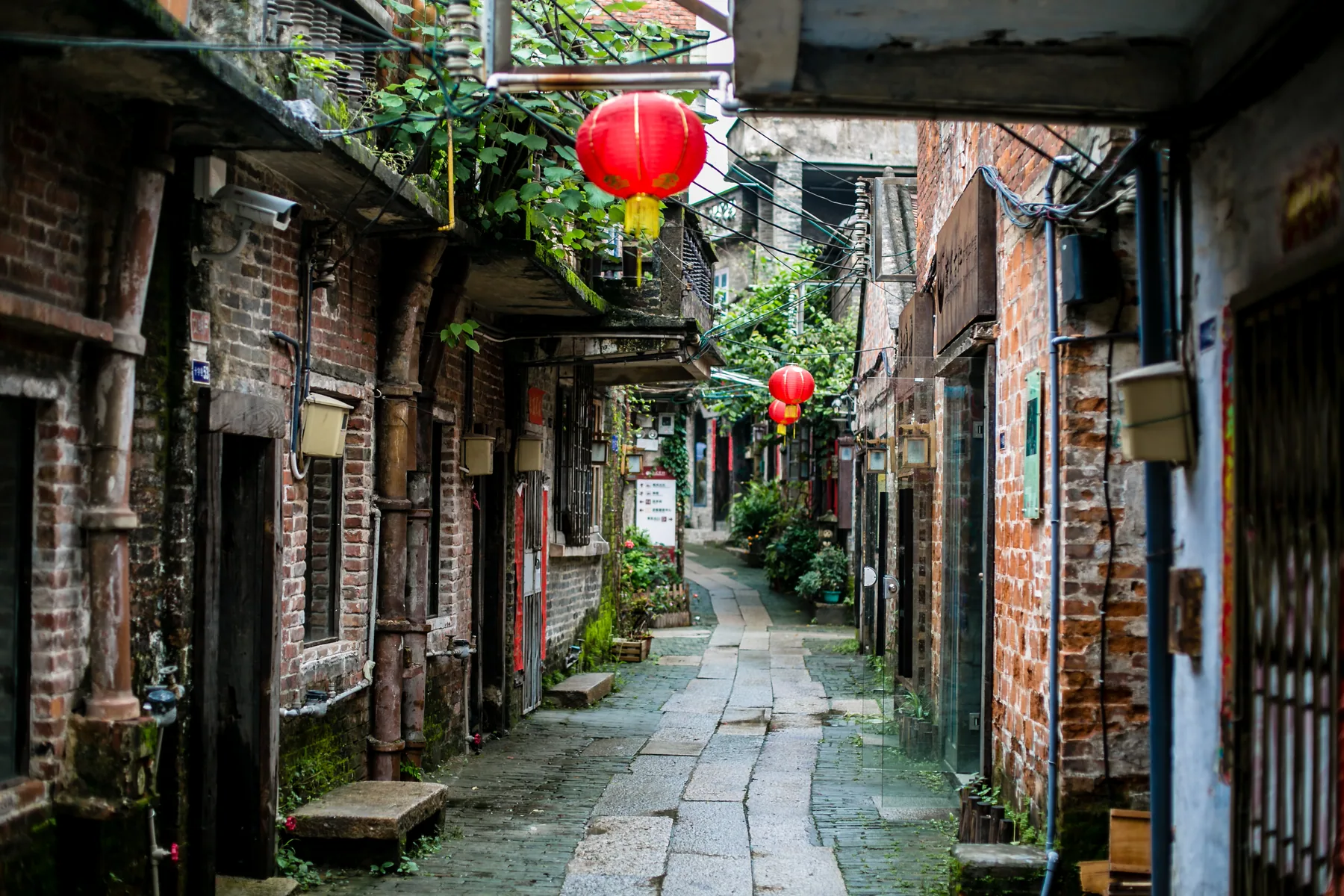 A narrow old Guangzhou lane with brick walls, shopfronts, plants and red lanterns
