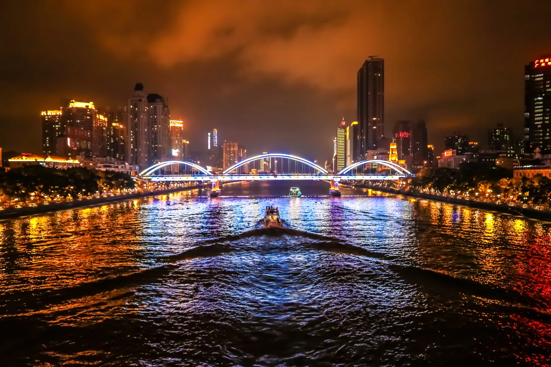 A night boat moving along the Pearl River beneath illuminated bridges and riverside buildings in Guangzhou