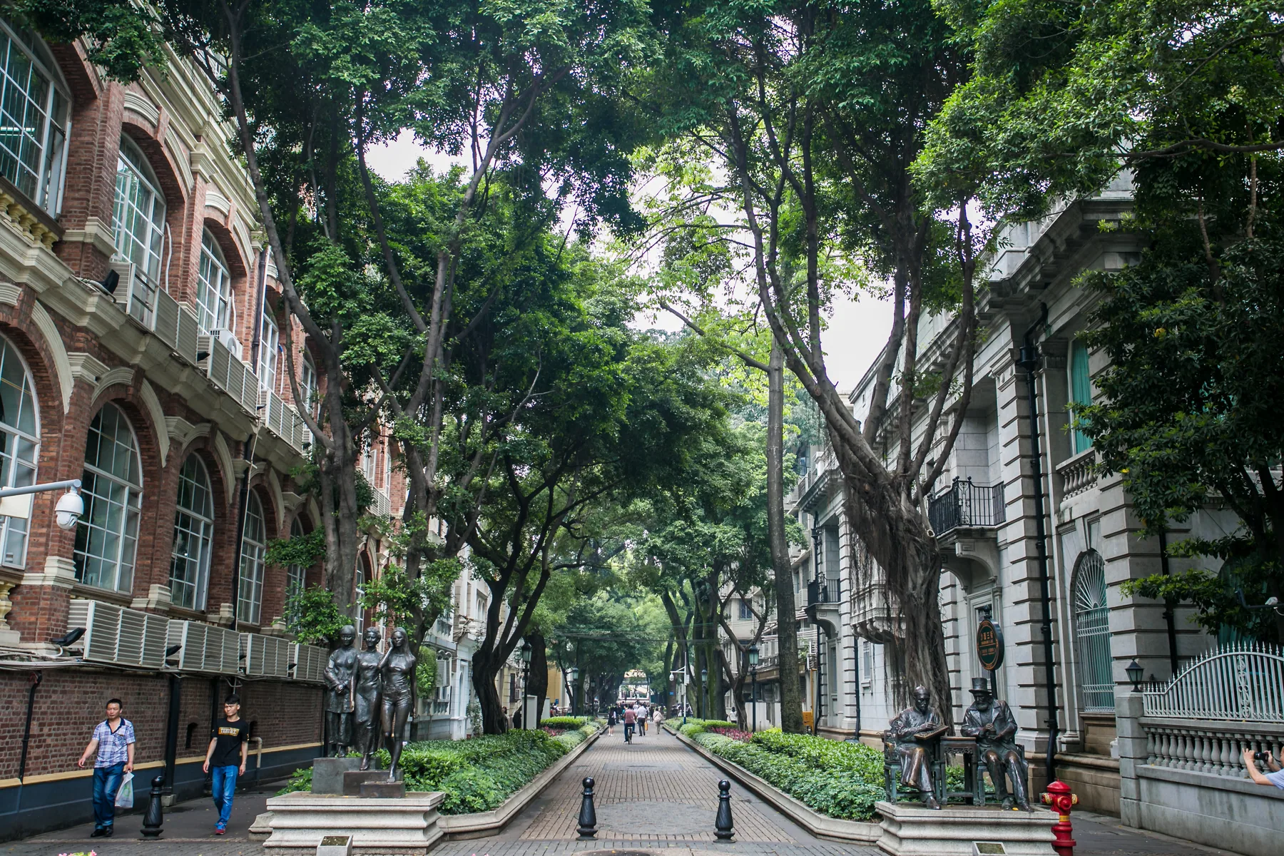 People walking beneath mature trees and historic facades on Shamian in Guangzhou