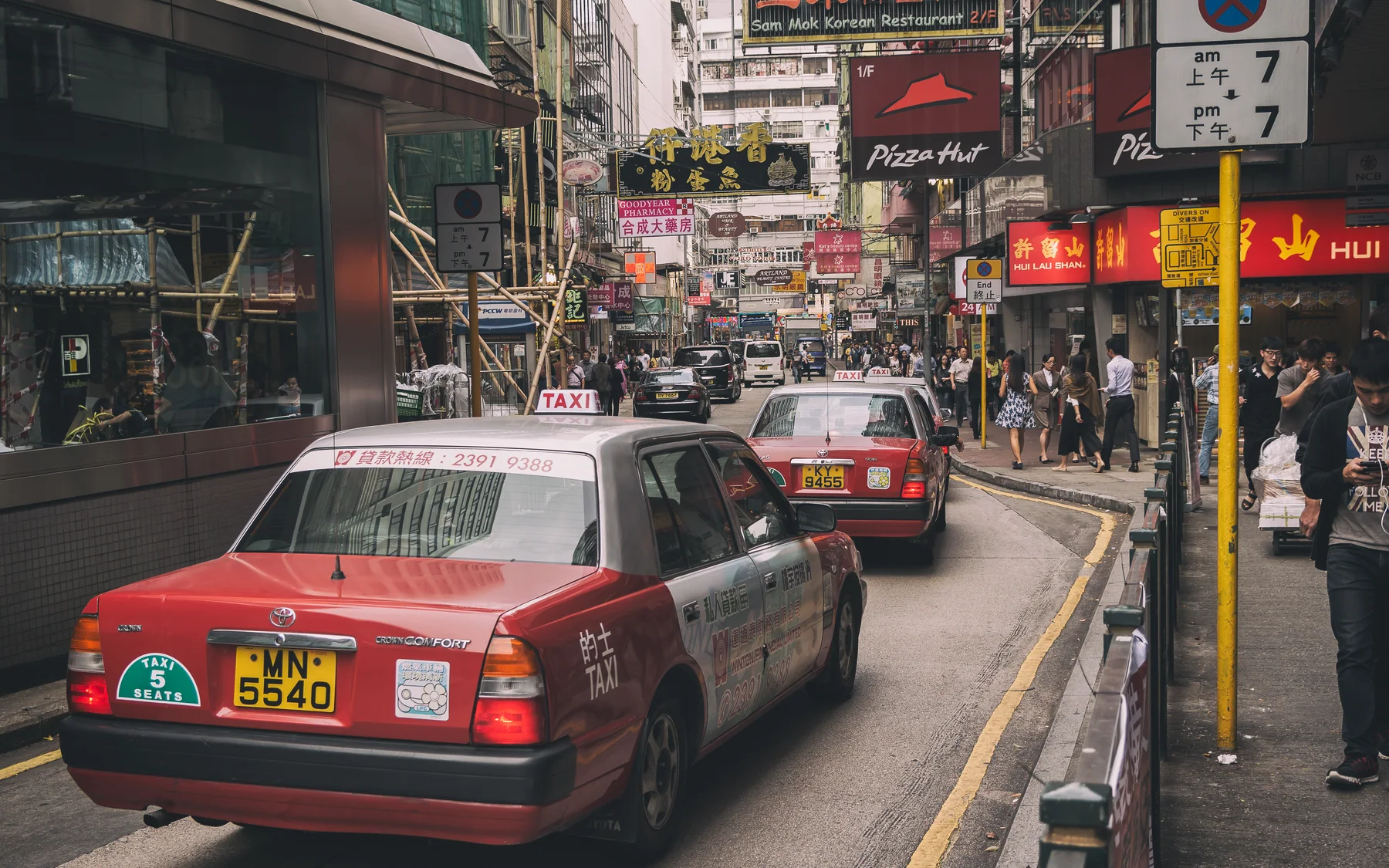 Red taxis, bilingual signs and a narrow Hong Kong street showing how road transport meets pedestrian density