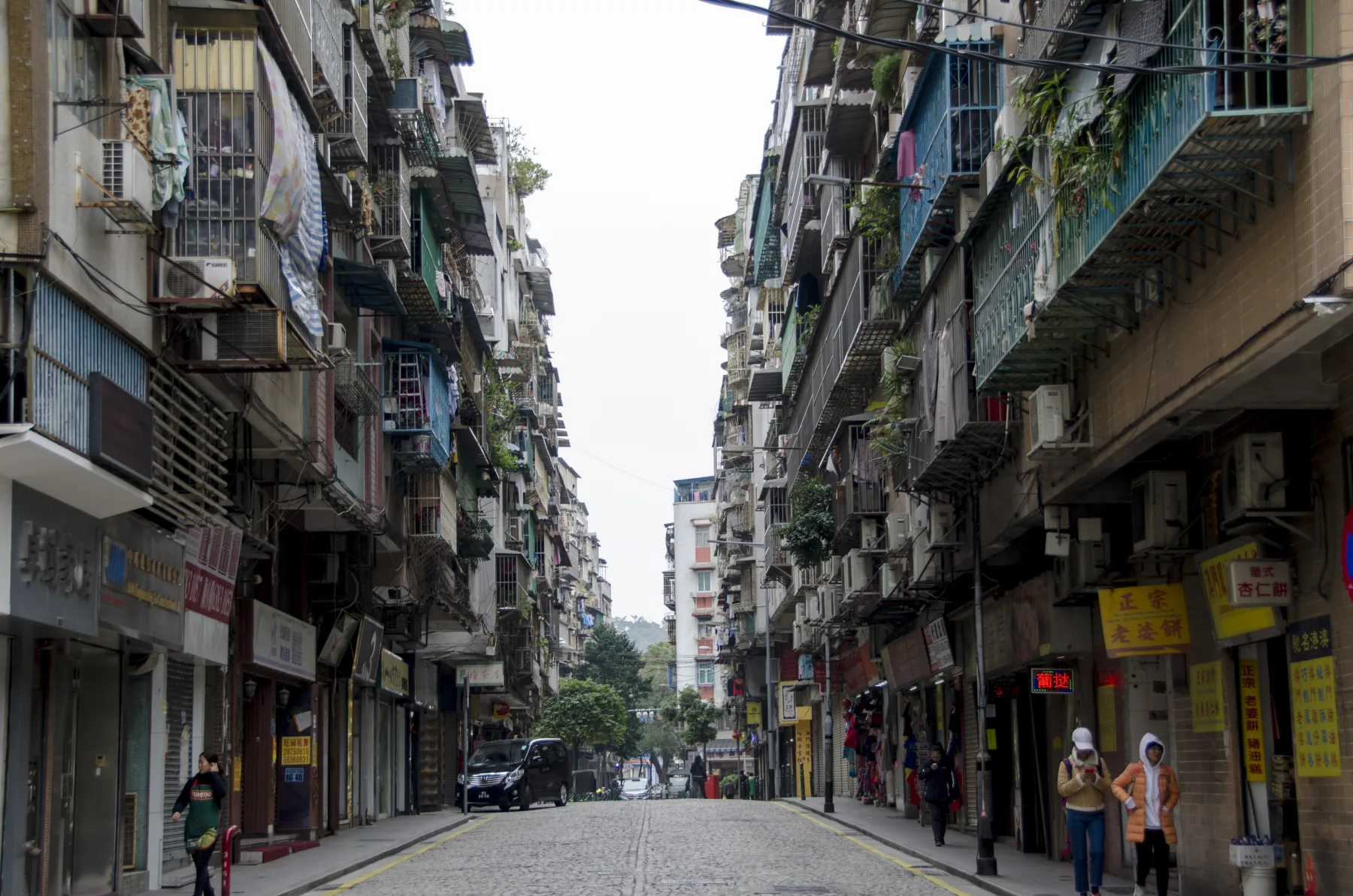A narrow residential and commercial street showing everyday urban life in Macau