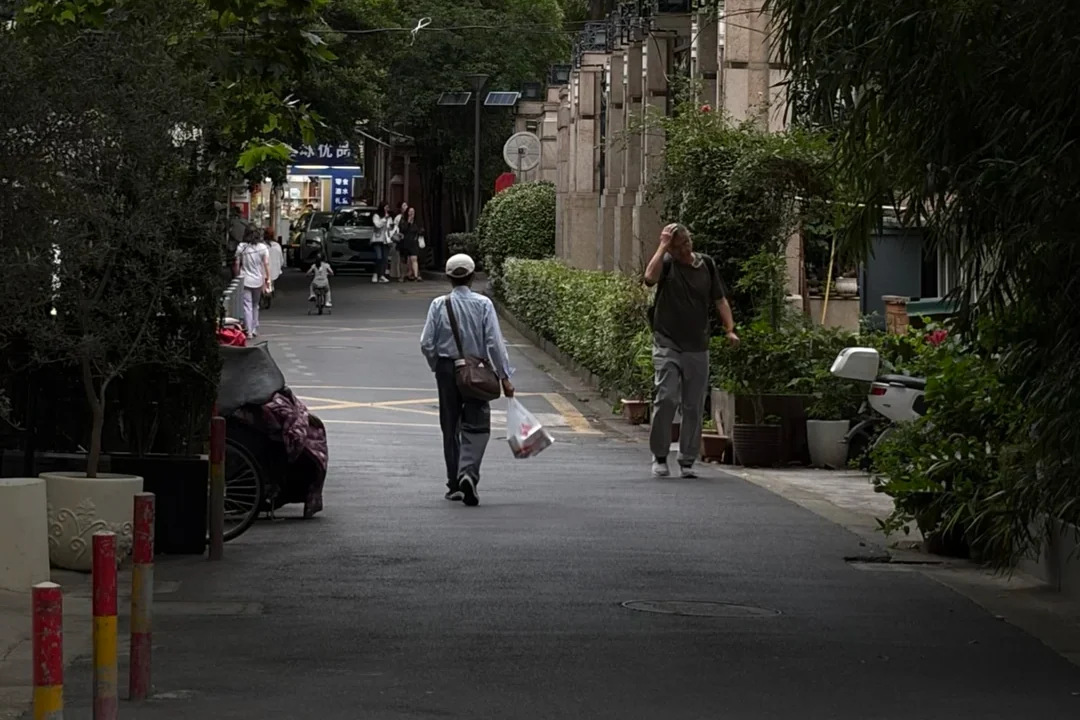 A public, plane-tree-lined Shanghai neighborhood street where walking speed reveals gates, deliveries and ordinary circulation