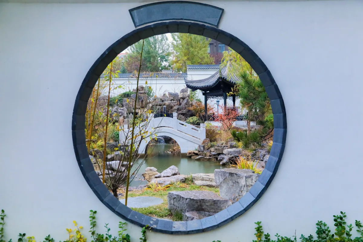 Circular window framing a bridge and water in a Suzhou garden
