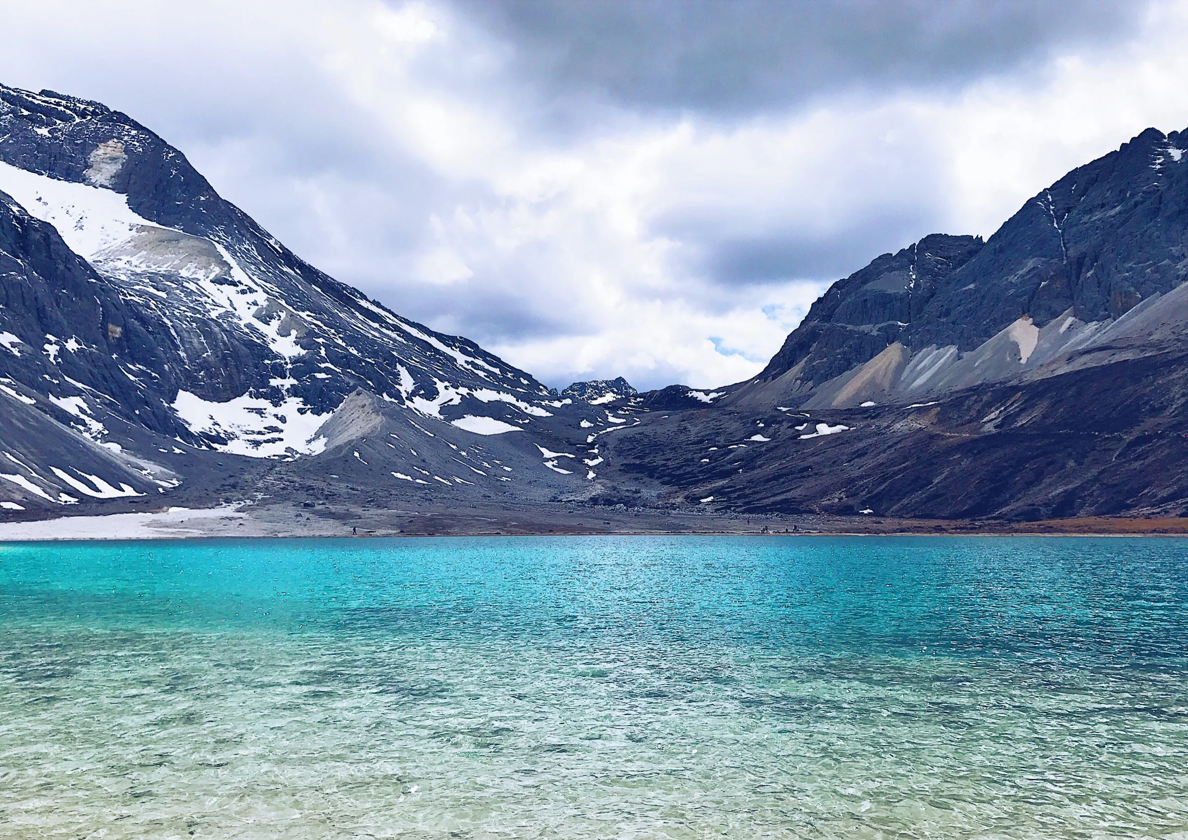 Turquoise Milk Lake beneath steep snow-streaked mountains in Daocheng Yading