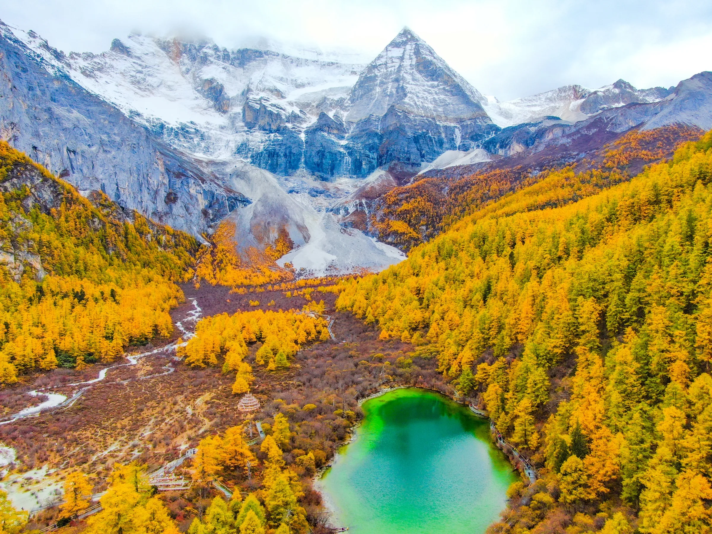 Pearl Lake and autumn forest below snow mountains in Daocheng Yading