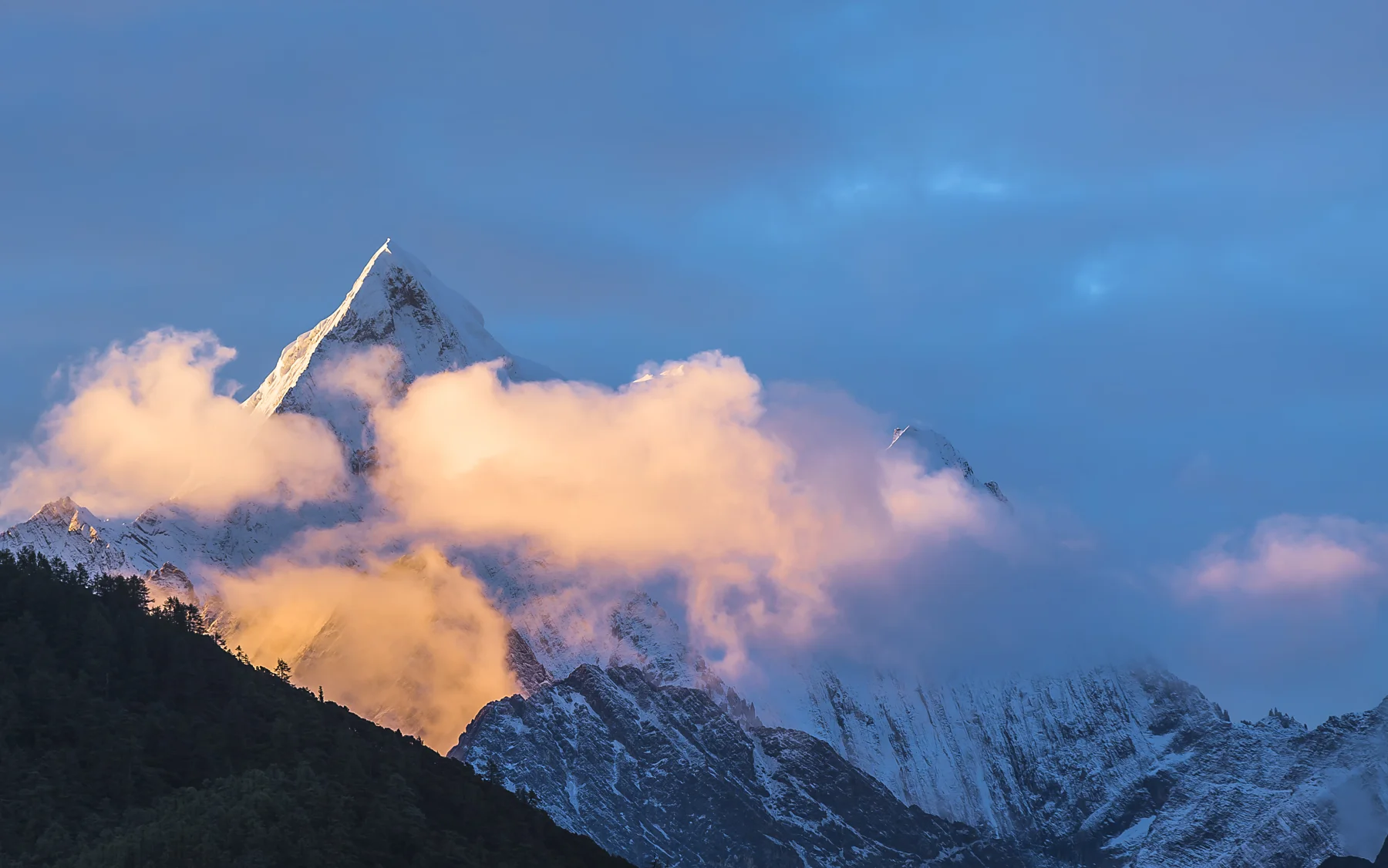 The sacred peaks of Daocheng Yading catching golden light beneath changing cloud