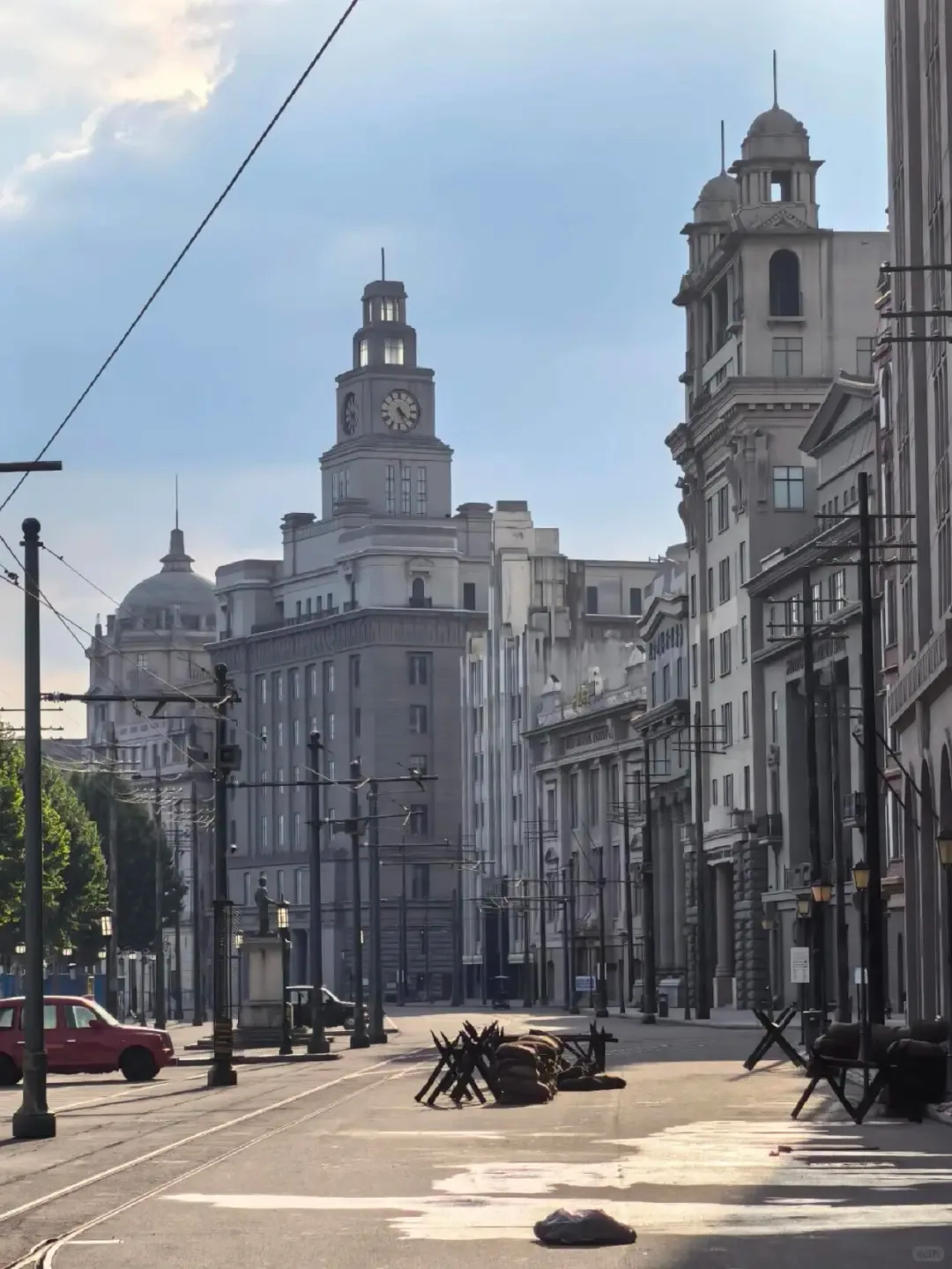 A broad daytime street of pale period facades with modern production space visible beyond