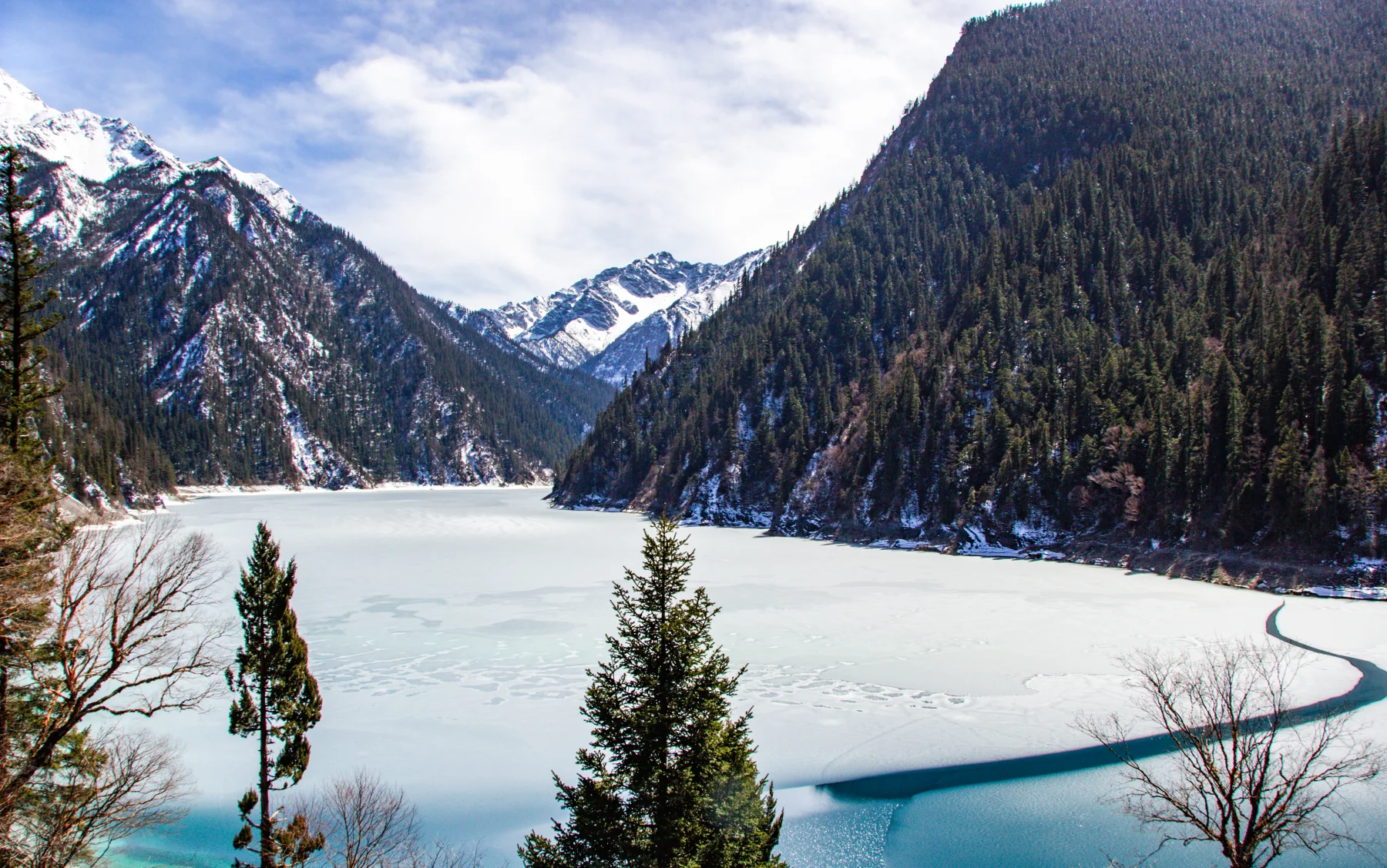A frozen Jiuzhaigou mountain lake surrounded by winter forest and snow peaks